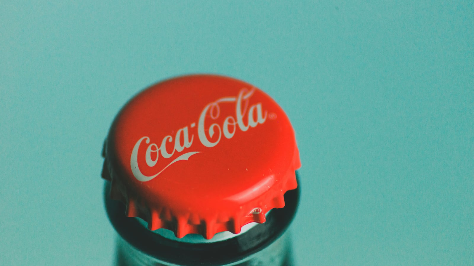 Close-up of a Coca-Cola bottle cap on a teal background