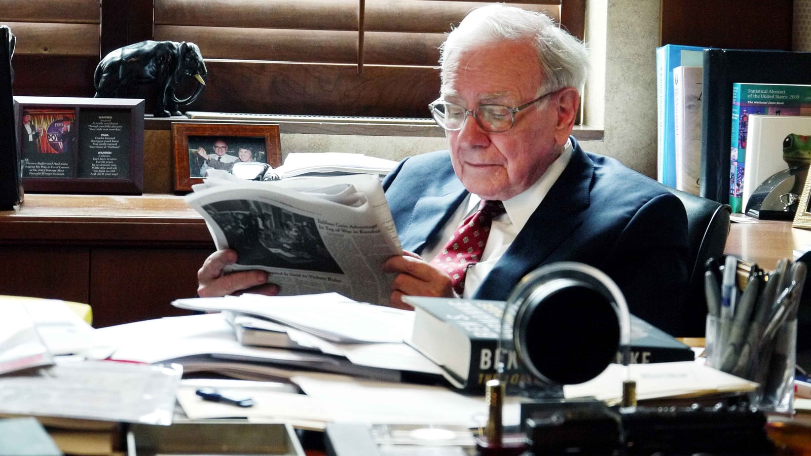 Warren Buffett reading a newspaper at his desk in Berkshire Hathaway's Omaha office